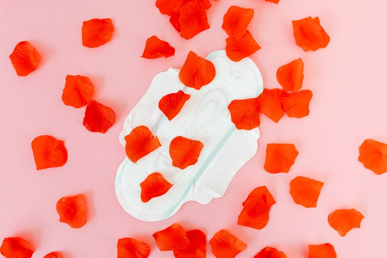 White sanitary napkin surrounded by red petals on a pink background, representing menstruation and feminine hygiene.